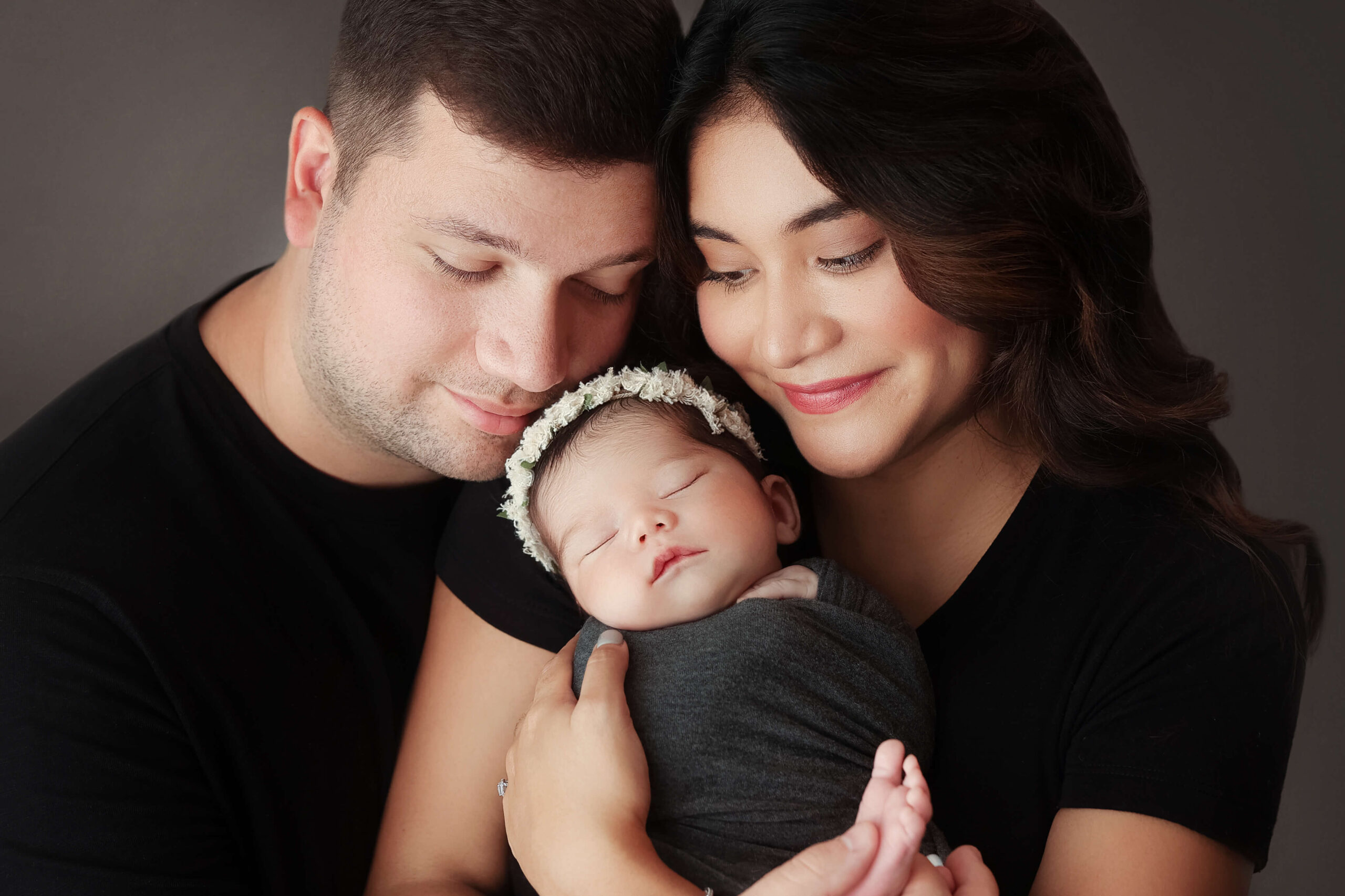 new parents with their eyes closed holding their newborn daughter in their family newborn pictures in a  newborn session