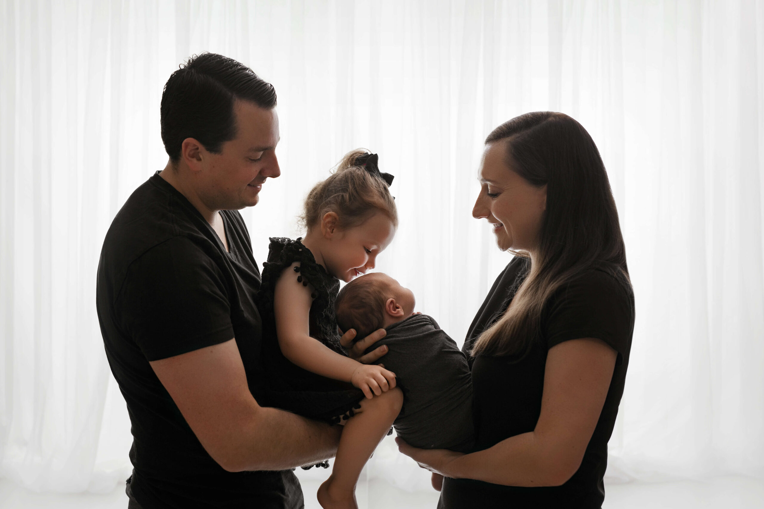 young mother and father and young 3 year old daughter with newborn baby boy wearing simple outfits in their family newborn pictures