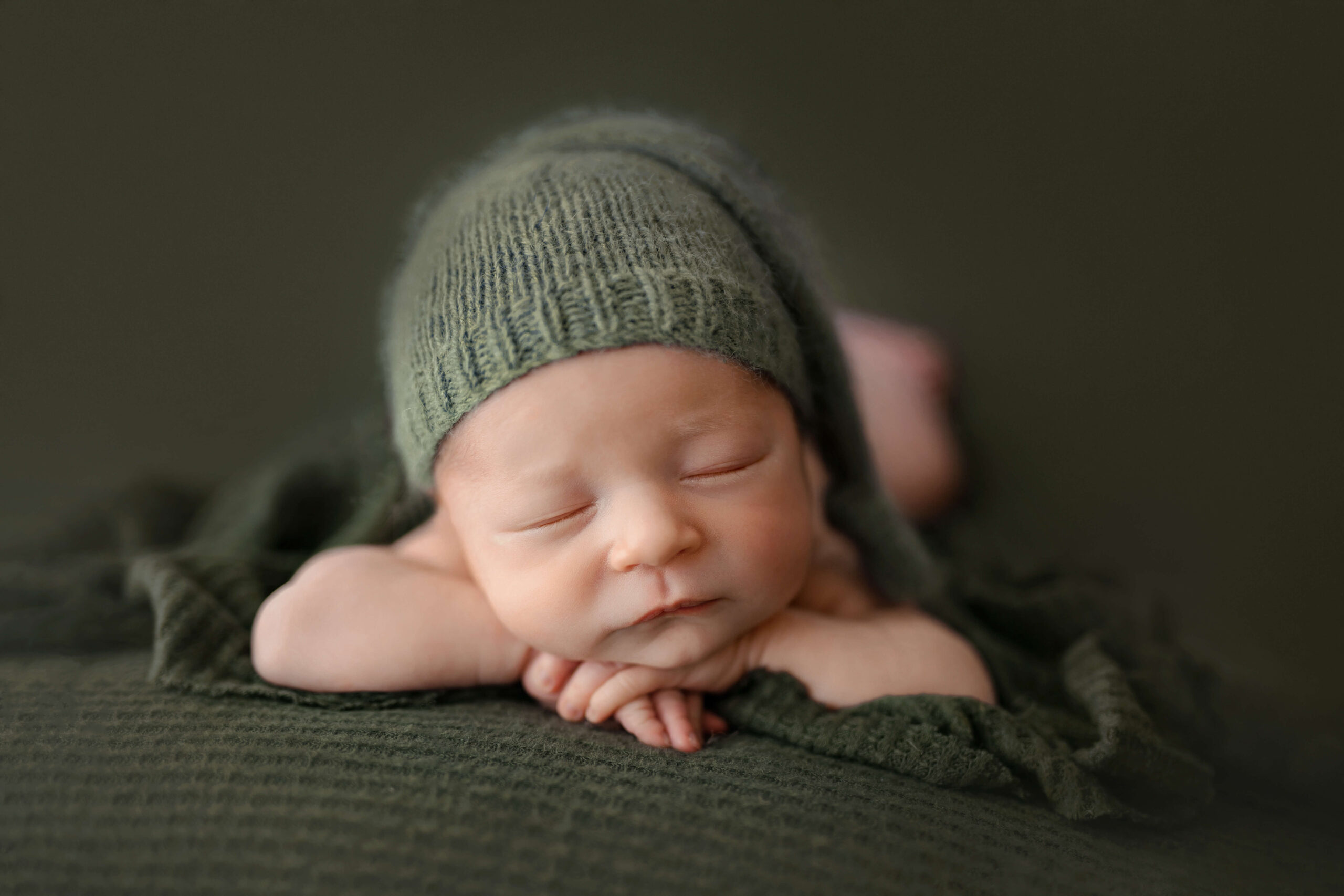 newborn baby laying on a green blanket with a matching sleepy cap taken in a professional newborn photography session, do you really need newborn photos