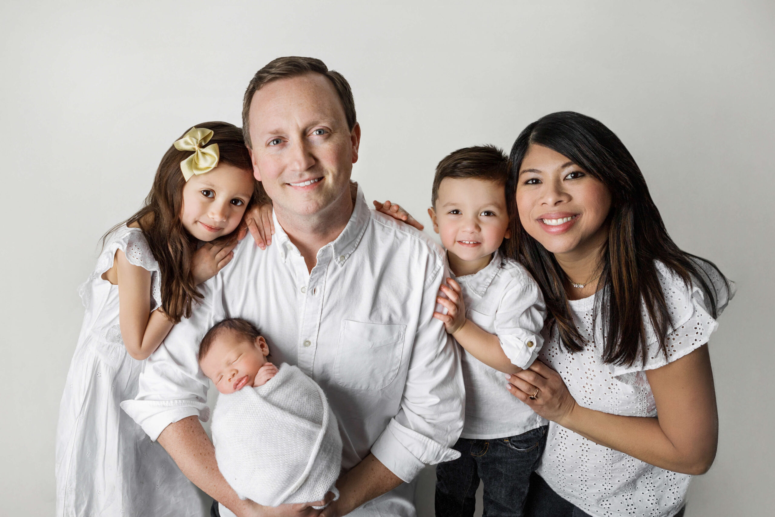 mom, dad, bug brother, big sister and newborn baby wearing white smiling hugging each other during their family newborn pictures in their newborn session