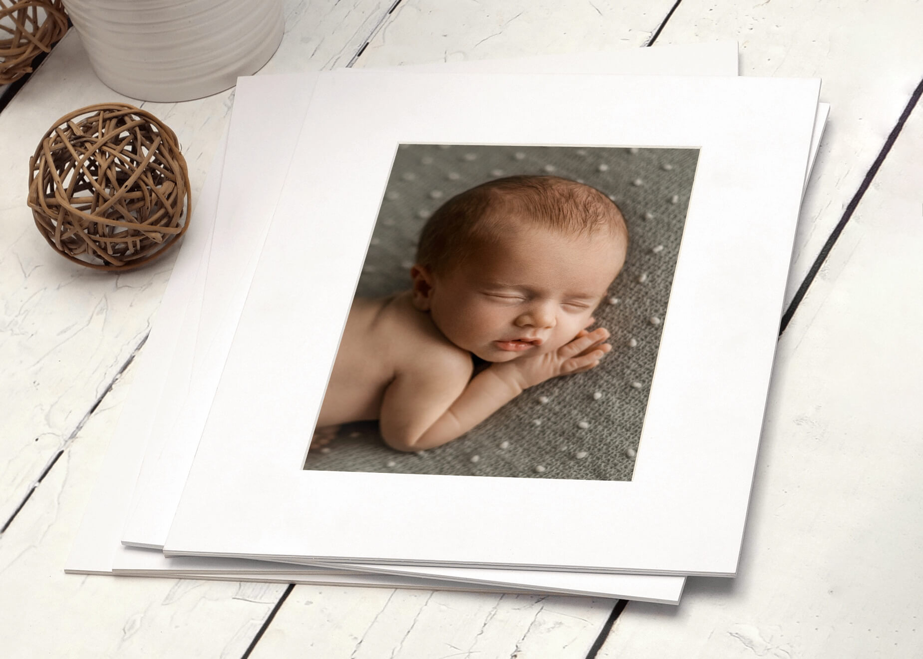 matted print of a newborn baby sitting on a white wood floor printed by a professional photographer