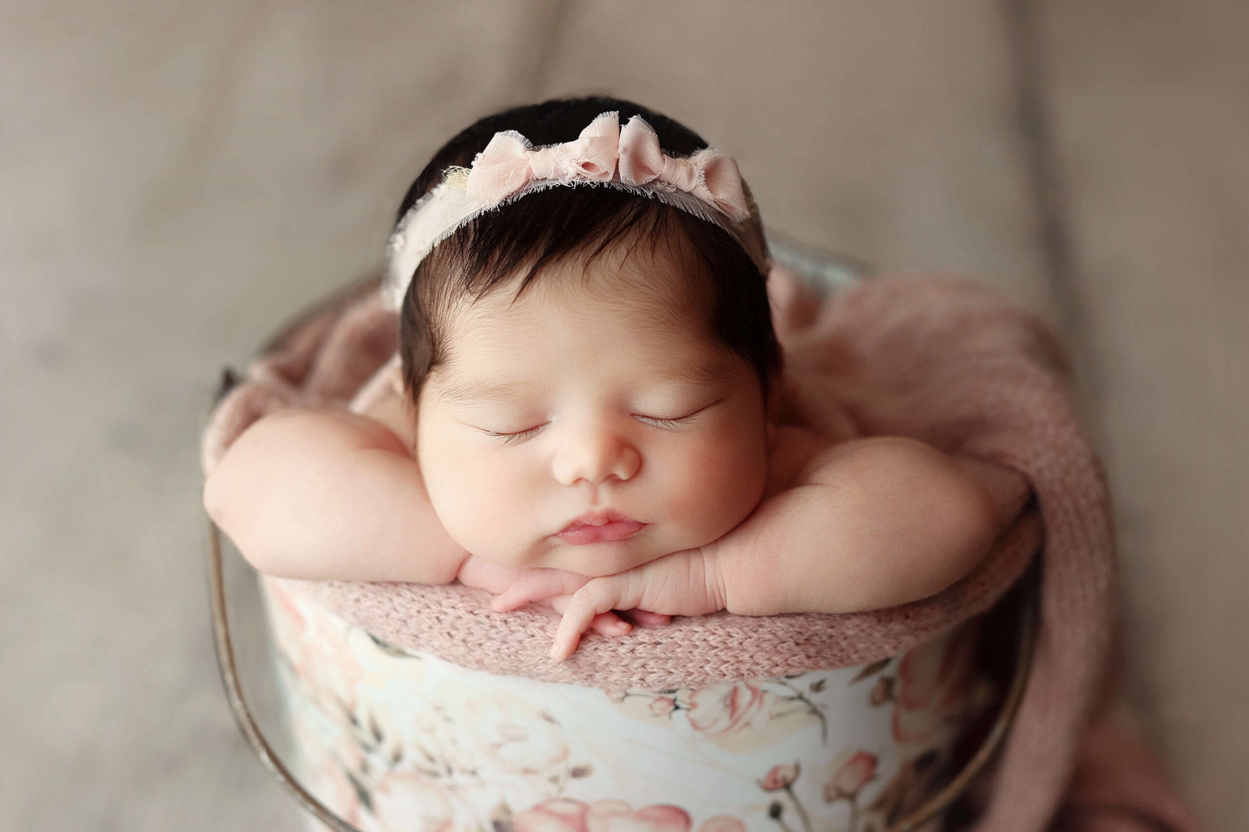 newborn baby girl in a pink floral bucket with a headband at her newborn session in Sterling VA