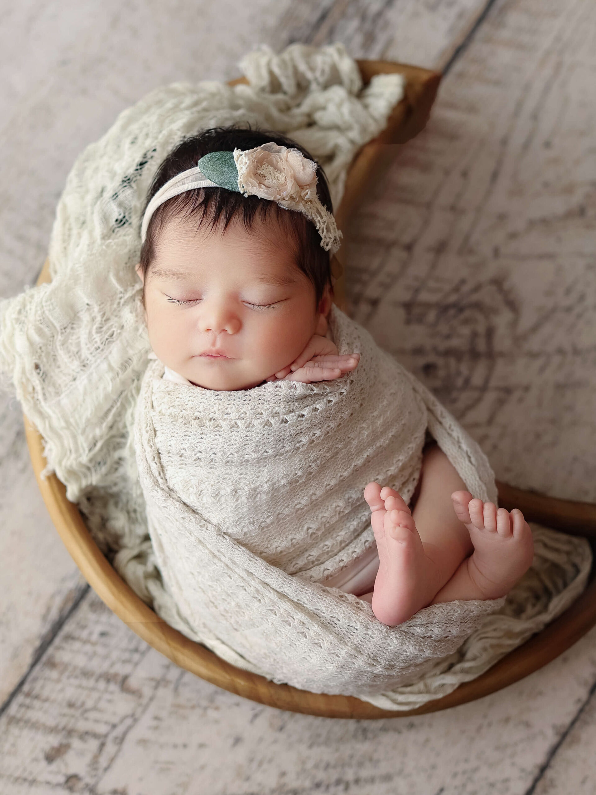 newborn photo taken by a Loudoun VA baby photographer, infant in a wrap and headband laying in a wooden moon shaped bowl at a baby photo shoot