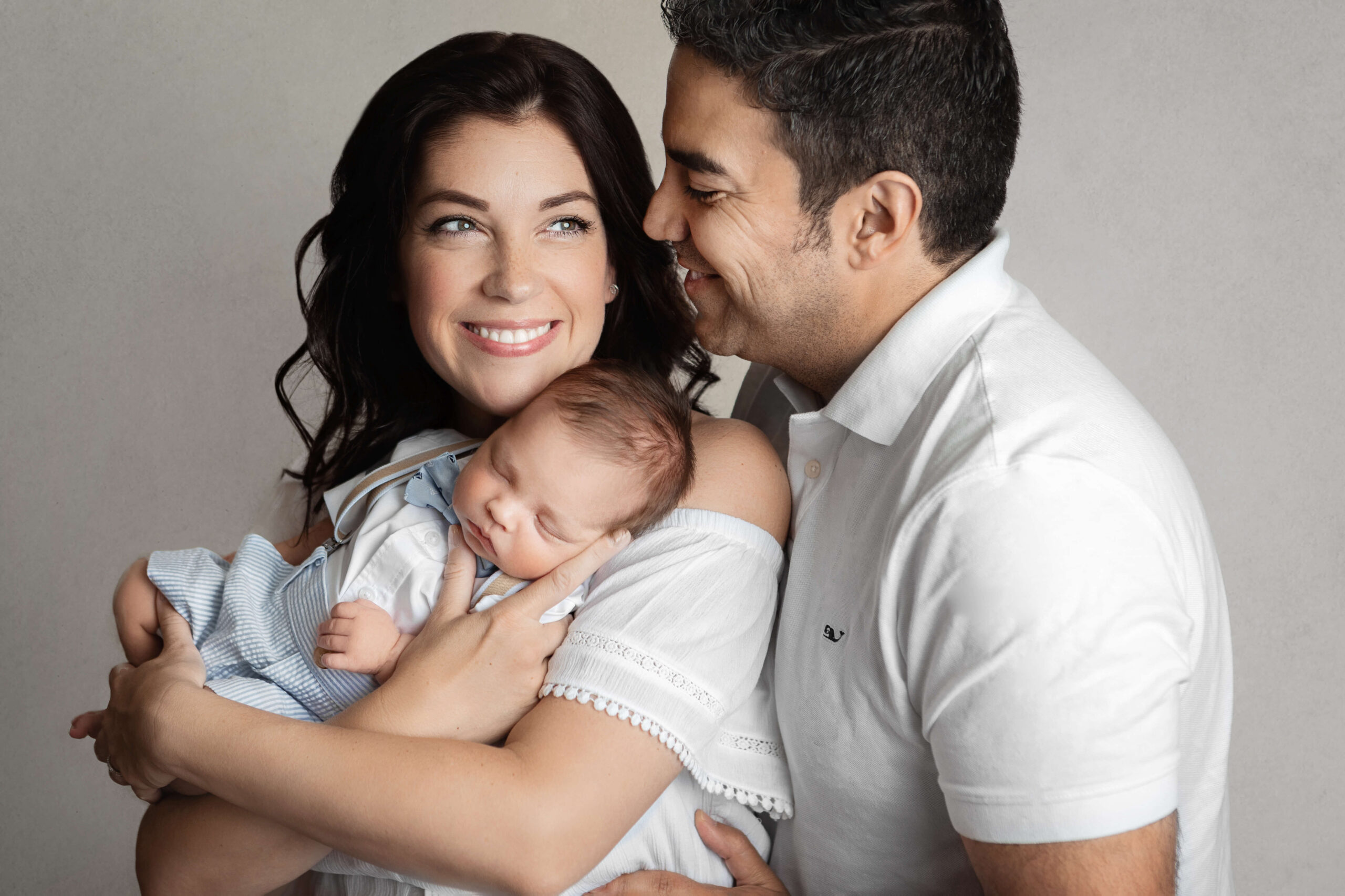newborn parent image taken at a family newborn session, mom and dad wearing white tops holding their newborn baby boy in a cute outfit