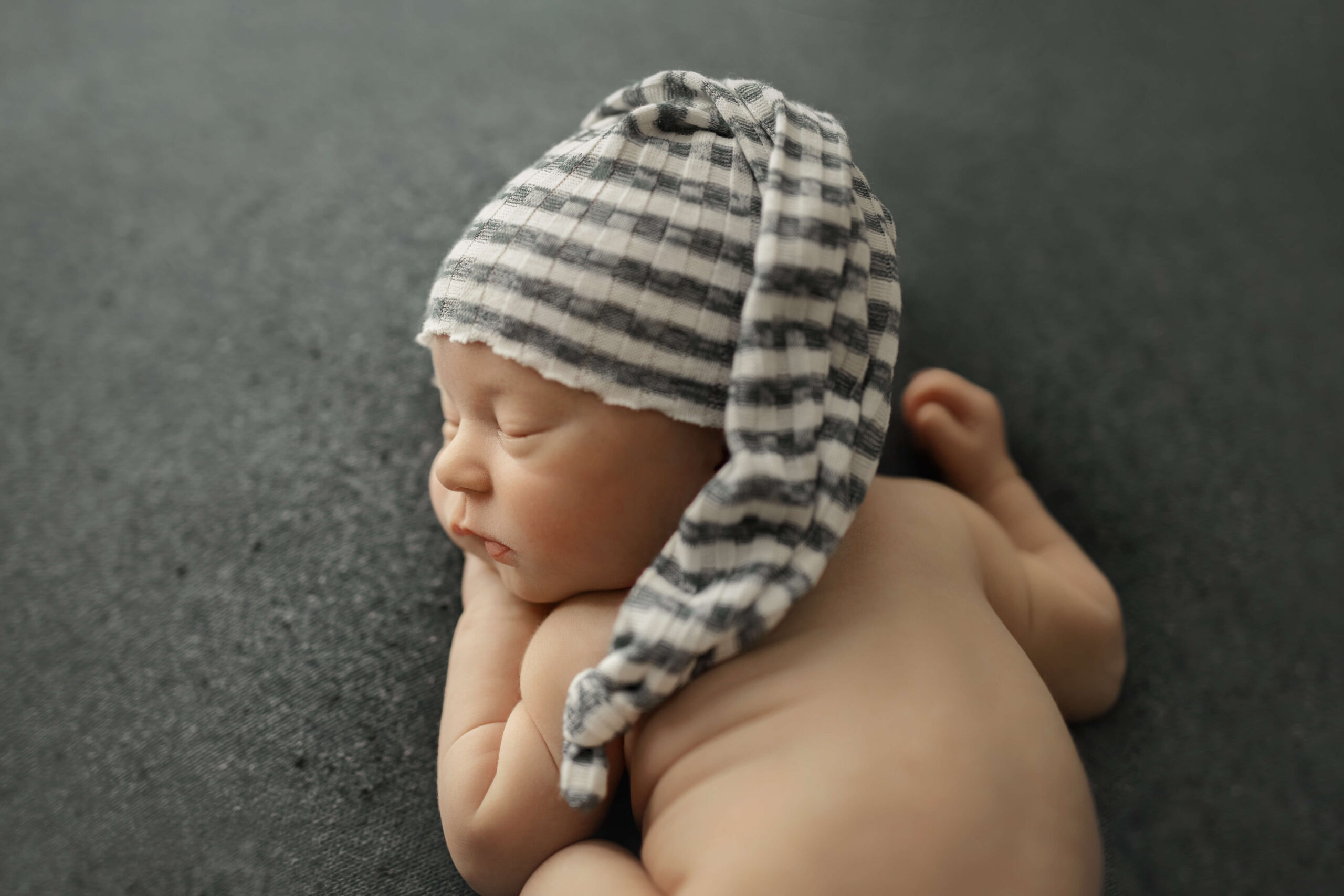newborn baby boy sleeping on a blue backdrop with a striped sleepy cap at his newborn session