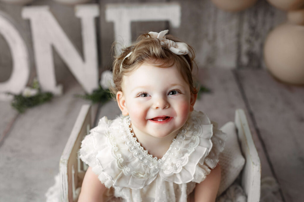 toddler in white outfit smiling at a Cake Smash Photo Shoot at a Fairfax VA Toddler Photography Studio