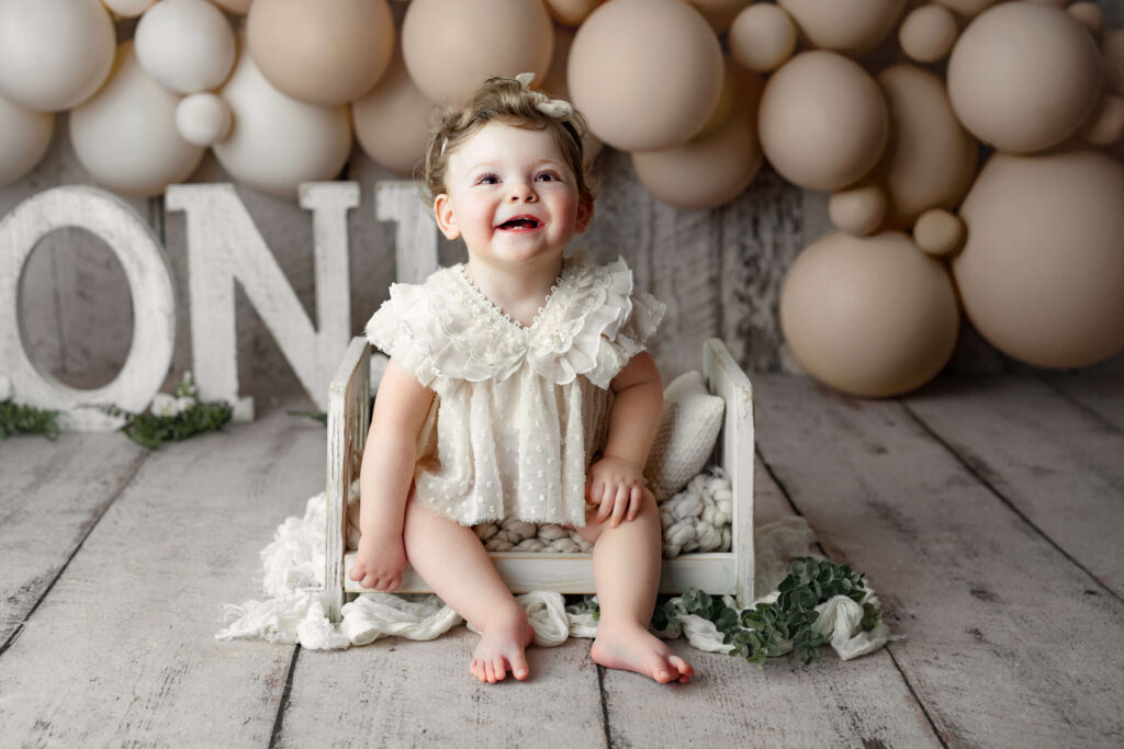 toddler in white outfit in wooden bed at a Cake Smash Photo Shoot at a Fairfax VA Toddler Photography Studio