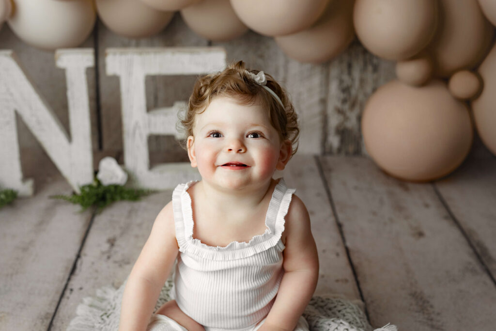 toddler in white onesie smiling at a Cake Smash Photo Shoot at a Fairfax VA Toddler Photography Studio