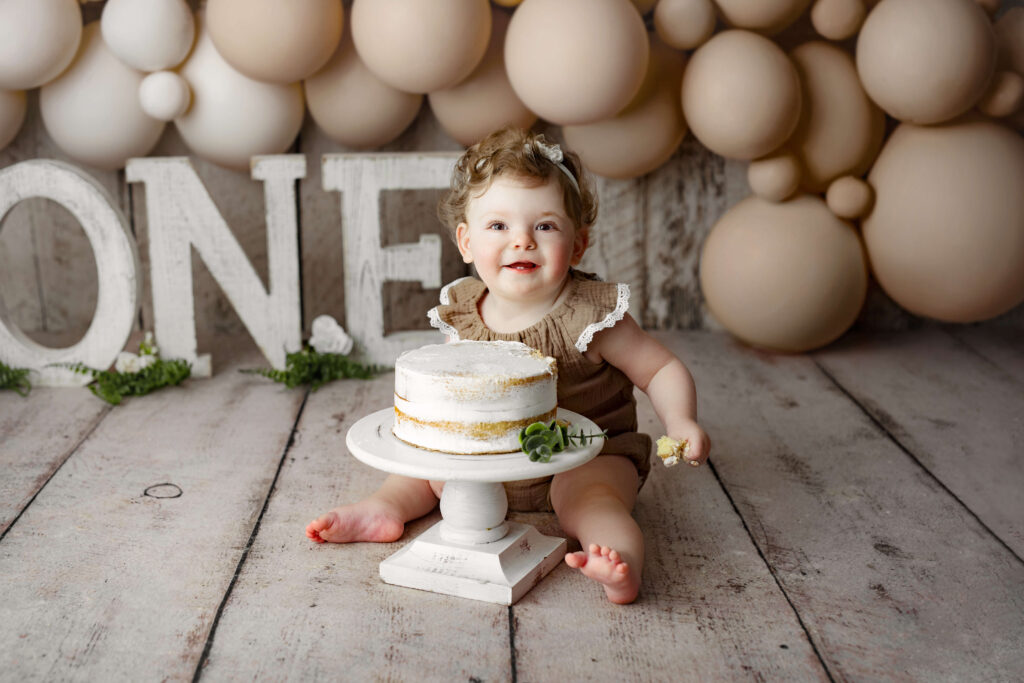 toddler in brown onesie in front of a birthday cake at a Cake Smash Photo Shoot at a Fairfax VA Toddler Photography Studio