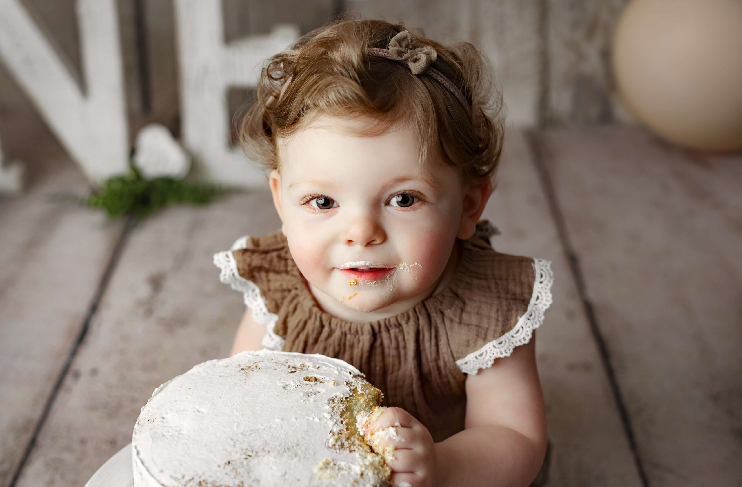 toddler in brown onesie eating a birthday cake at a Cake Smash Photo Shoot at a Fairfax VA Toddler Photography Studio
