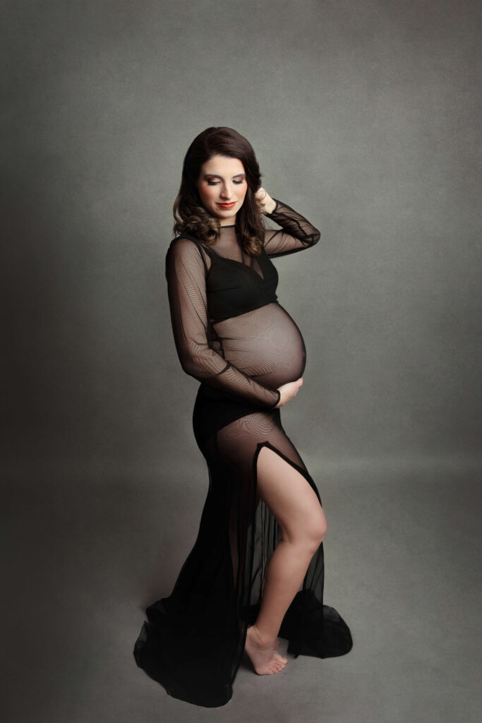 pregnant mother wearing a black maternity dress with a slit in her in studio maternity session in va by Maternity Photographer Tysons Corner VA