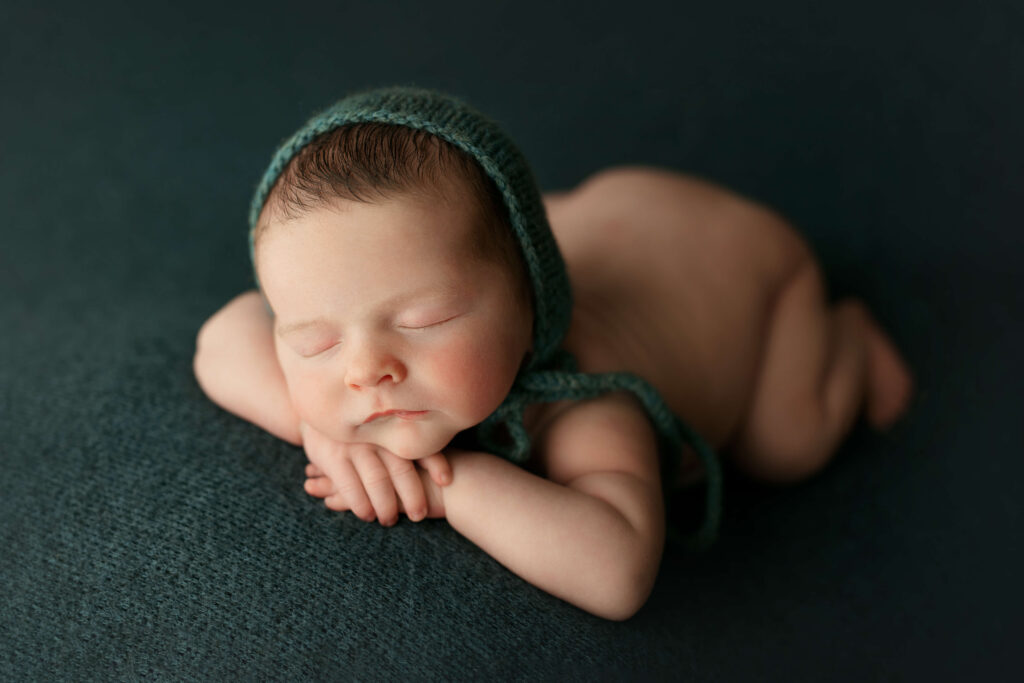 newborn in a head on hands pose on a teal backdrop taken by a Northern Virginia Newborn Photographer