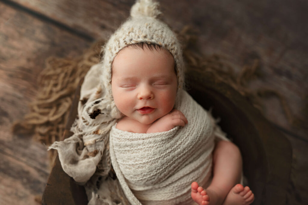 newborn in a white knit wrap and pom bonnet in a wooden bowl taken by a Northern Virginia Newborn Photographer
