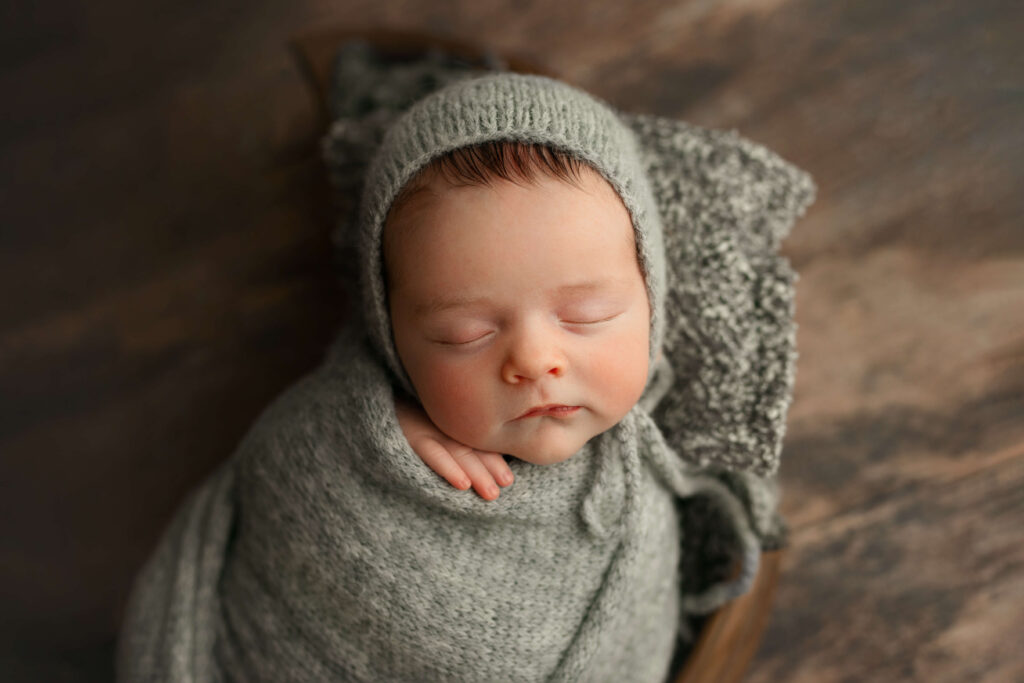 newborn in a grey knit wrap in a moon wooden bowl taken by a Northern Virginia Newborn Photographer