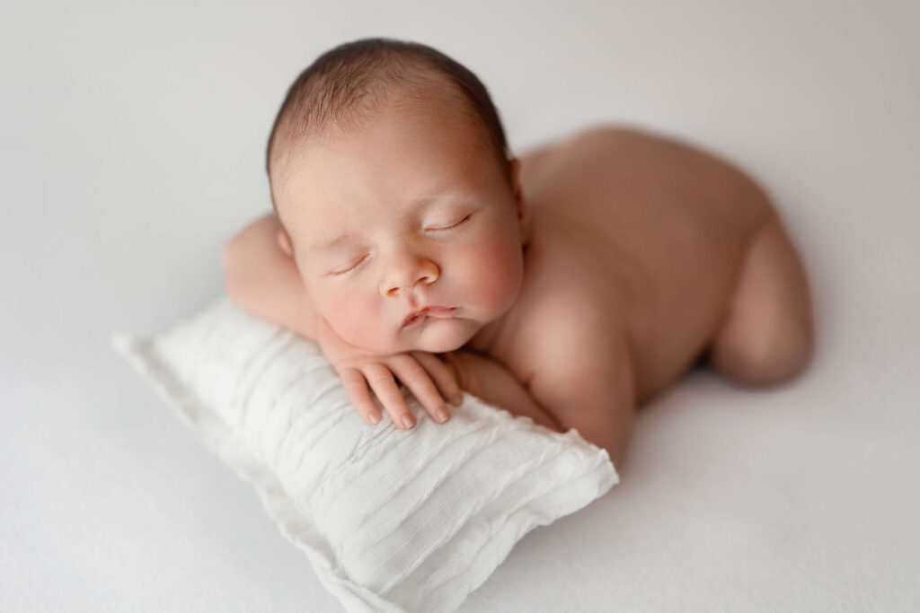 newborn baby naken on a white background with white pillow taken by an ashburn va newborn photographer