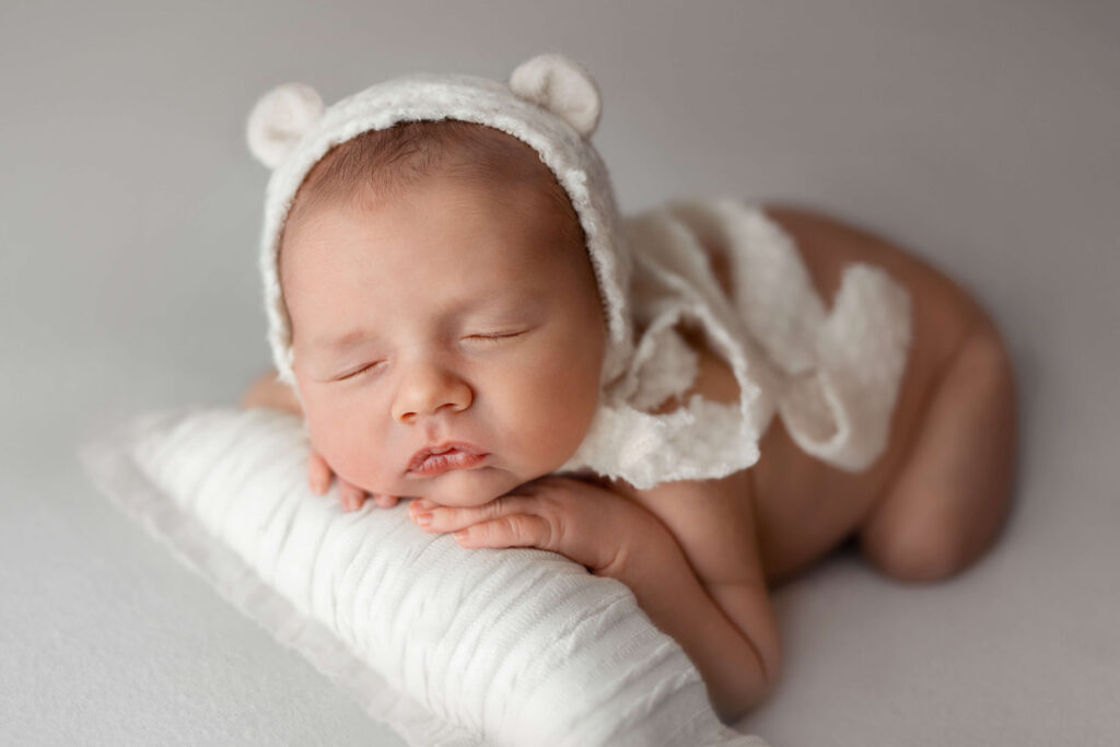 newborn baby naked on a white background with a bear bonnet on white pillow taken by an ashburn va newborn photographer
