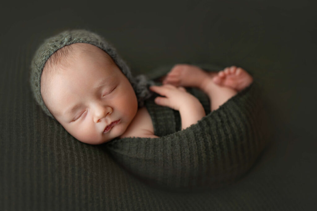 newborn baby laying on green background with green wrap and bonnet