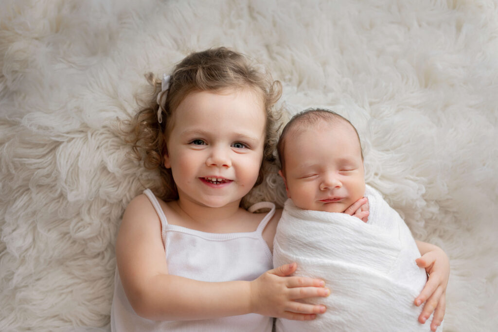 big sister laughing holding her newborn baby brother taken by an ashburn va newborn photographer