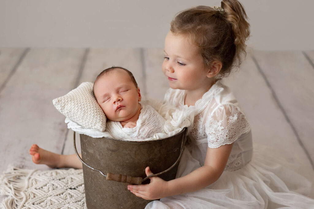 big sister looking at her newborn baby brother in a bucket