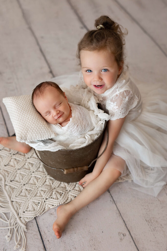 big sister laughing next to her newborn baby brother in a bucket