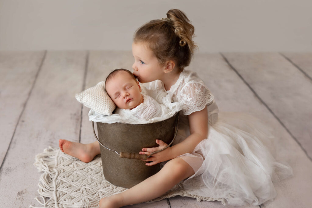 big sister kissing her newborn baby brother in a bucket