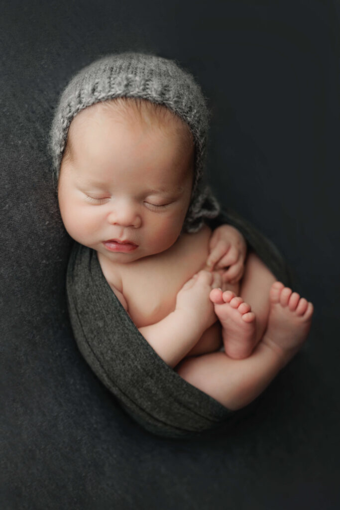 baby on a grey backdrop with a grey bonnet newborn photography dc