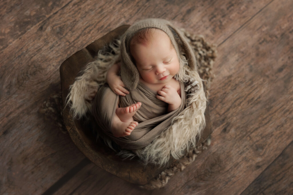 newborn baby on a wooden bowl with a bunny bonnet